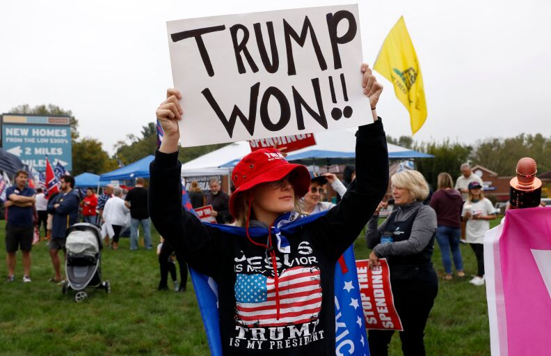 A person in a field holds a sign reading: Trump Won!!
