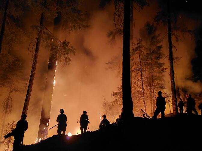 Firefighters are silhouetted on ridge with the sky full of red smoke