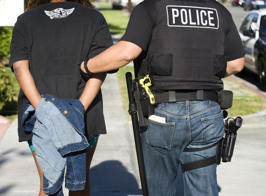 After arresting Toya Latrice Daniels,  Buena Park police officer James Woo, left, walks Daniels in his patrol car for transportation to the Buena Park Police Department. Daniels was charged with one misdemeanor count of contributing to the delinquency of a minor and one misdemeanor count of failure to reasonably supervise or encourage school attendance. By March of the school year, her elementary school child had accumulated 17 unexcused absences.