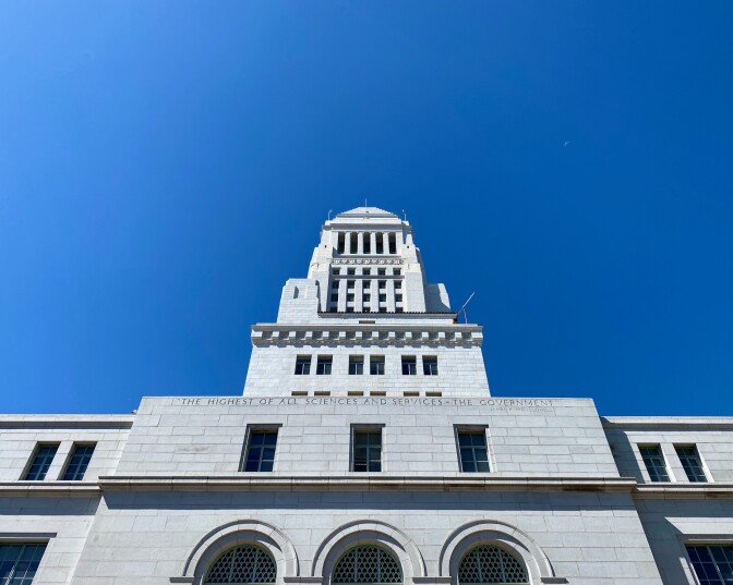 An image of Los Angeles City Hall against a blue sky from the perspective of someone looking up.