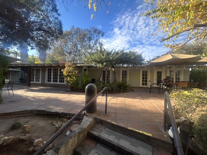A picture of a stairs leading up to a big patio then a ranch style home.