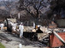 Workers in white suits covering their entire body and face masks remove debris from a burnt home.