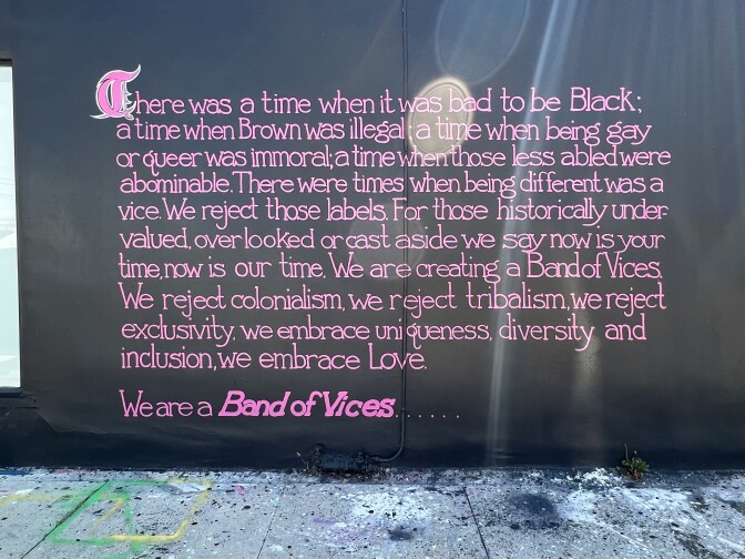 A mural painted black with pink letters that says: There was a time when it was bad to be Black; a time when Brown was illegal; a time when being gay or queer was immoral; a time when those less abled were abominable. There were times when being different was a vice. We reject those labels. For those historically undervalued, overlooked or cast aside we say now is your time, now is our time. We are creating a Band of Vices. We reject colonialism, we reject tribalism, we reject exclusivity, we embrace uniqueness, diversity and inclusion, we embrace love.