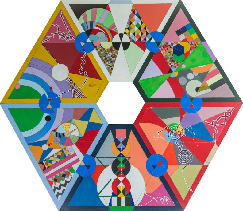A colorful piece of art made up of a diverse array of geometric shapes in a wide variety of colors. The overall pattern forms a hexagon with a hole in the center, made up of trapezoids, with further geometric shapes within. These include small hourglasses, circles, zigzag patterns, and much more.