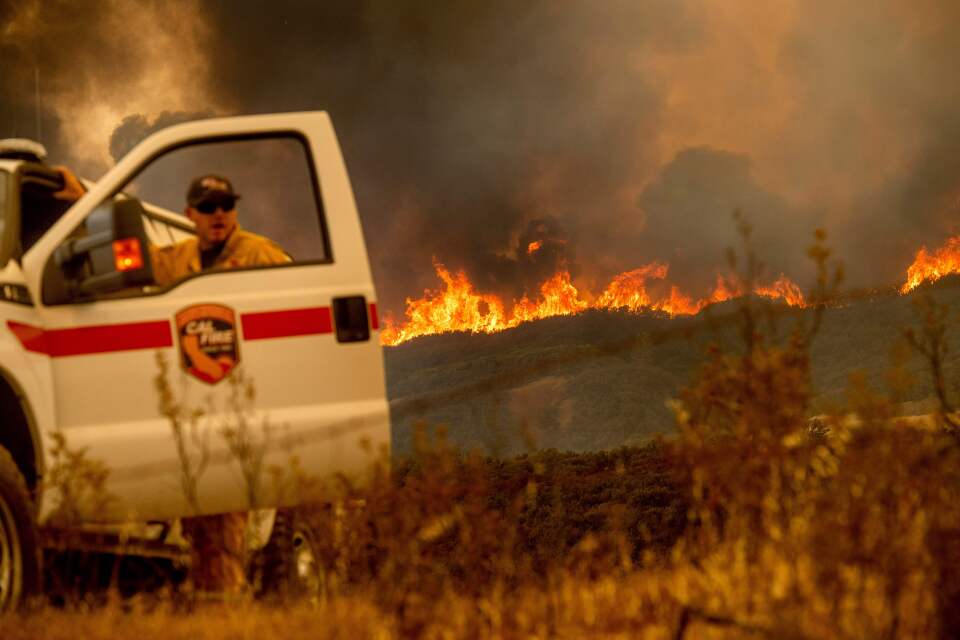 The Ranch Fire, part of the Mendocino Complex Fire, crests a ridge as Battalion Chief Matt Sully directs firefighting operations on High Valley Rd. near Clearlake Oaks, California, on Sunday, Aug. 5, 2018. (Photo by NOAH BERGER / AFP)        (Photo credit should read NOAH BERGER/AFP/Getty Images)