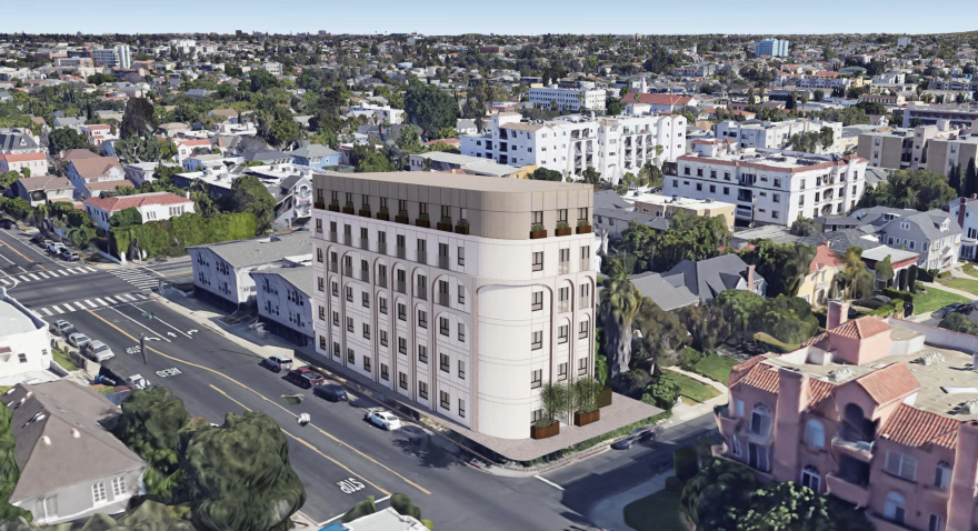 A six-story building with rounded corners sits on a coner next to smaller residential units