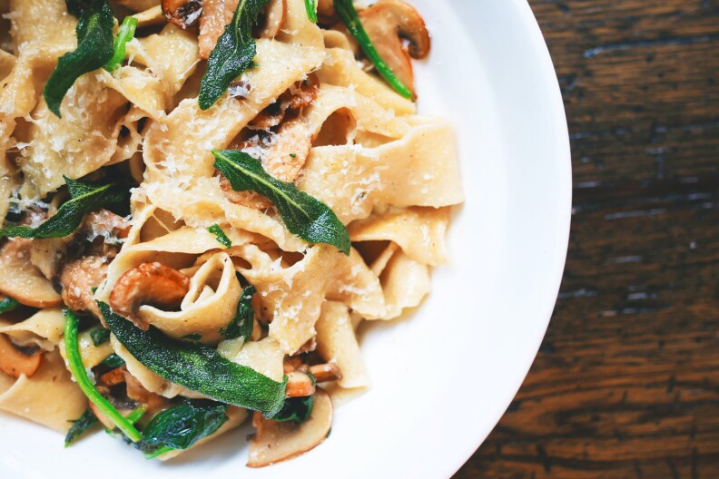 A bowl of pasta with mushrooms, greens and cheese.