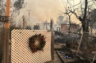 A burned down home with a white fence remaining where a Christmas wreath hangs. 