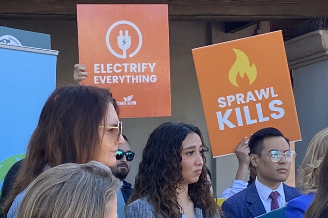 A close-up of a small group of people, two of them holding signs that say "Electrify Everything" and "Sprawl Kills."