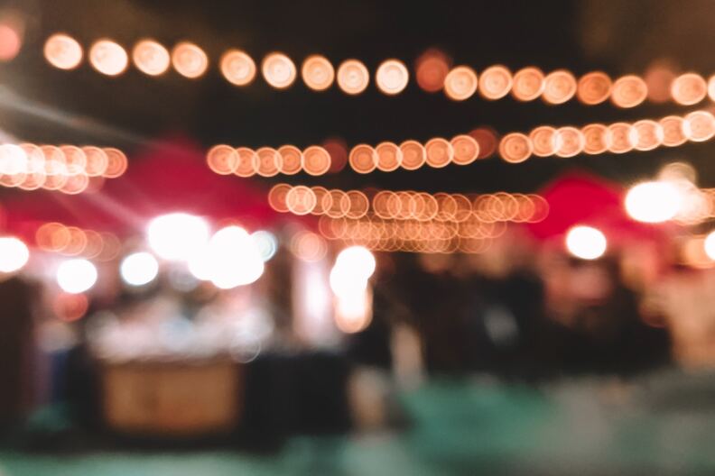 A blurry photo of a night market, strung with lights across the top.