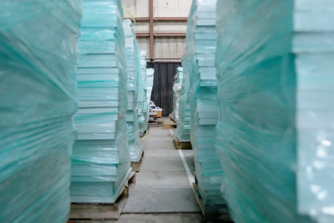 Several rows of solar panels wrapped in blue plastic are stacked high on pallets