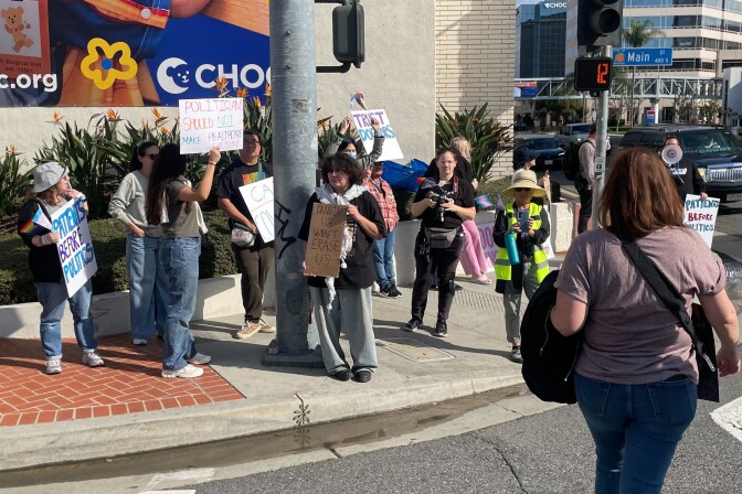Protesters on a street corner hold signs with slogans that include "Politicians should not make healthcare decisions," "Patients before politics" and "Trust doctors."