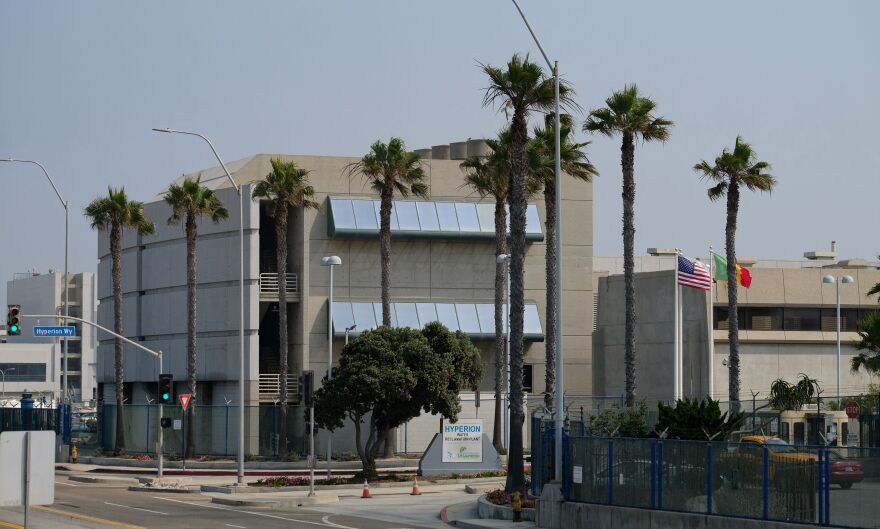 A multi-story building has a beige exterior and tall palm trees around it