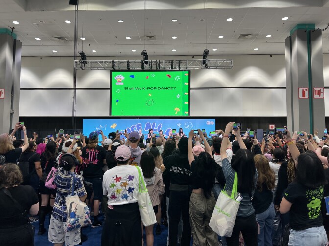A crowd of people hold up phones towards a group of performers on a stage. 