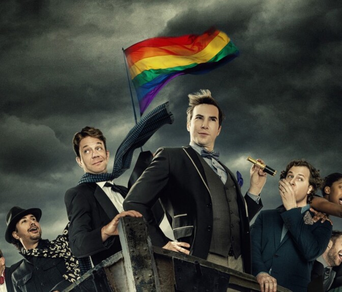 People on a boat flying the rainbow Pride flag. Three men at the front are dressed in suit jackets. One wears a scarf. One has a bow tie and holds a tiny telescope in one hand.