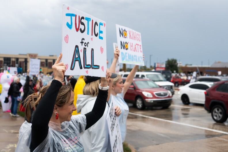 Protesters stand in the rain as cars drive by.