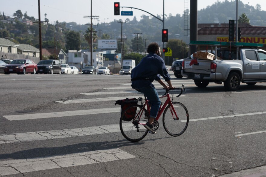 A person rides a red road bike through a busy intersection close to car traffic.