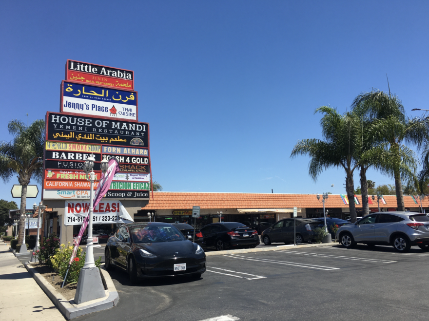 A sign with business names above a mini-mall parking lot.