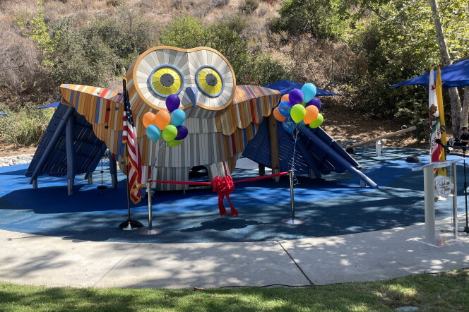 A 12-foot owl-shaped playground is seen on a rubber mat surface, surrounded by grass, balloons and vegetation.