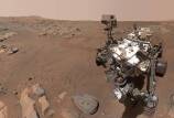 A selfie style image from NASA’s Perseverance Mars rover shows the rover to the right with the Martian landscape in the background.