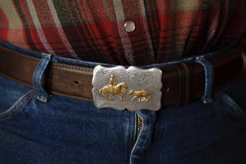 a belt buckle shows a person in a cowboy hat riding a horse that is facing a cow