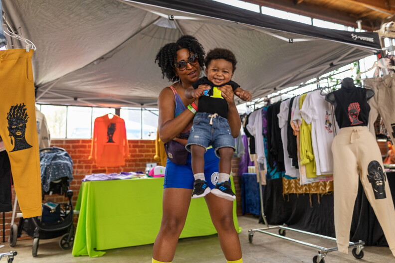 A woman holds her child up under a tent with merchandise in it.
