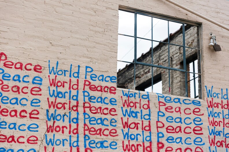 The words "world peace" are written in blue and red graffiti across a brick wall on a building.