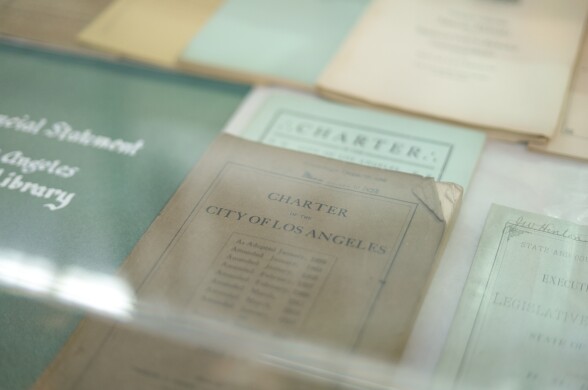 An old, worn book of the L.A. city charter from the 1920s in a display case. It's surrounded by other historic city documents.