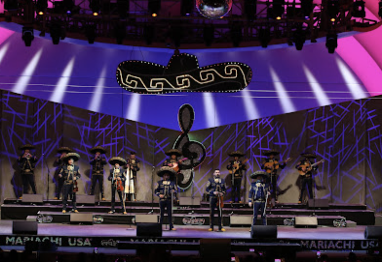 Performers in traditional black mariachi outfits play instruments on a purple-lighted stage.