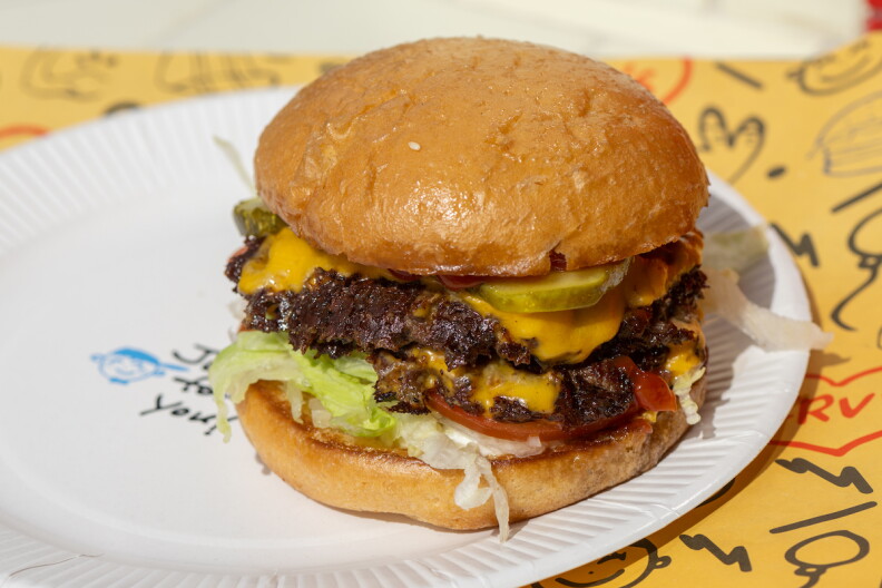 Irv's burger with two patties, cheese, pickles, lettuce, tomatoes on a paper plate.