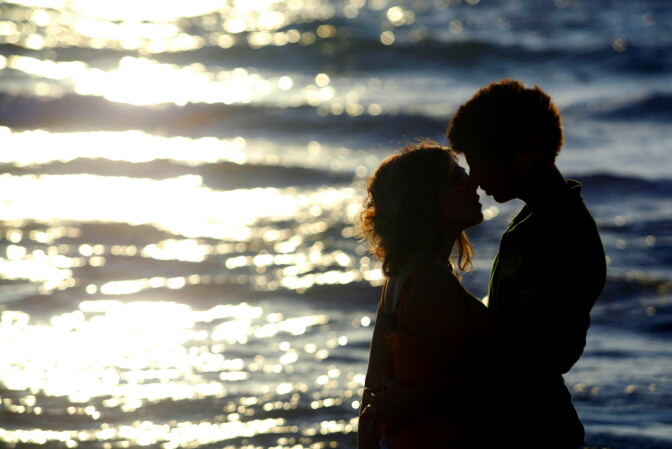 Two teenagers kiss in front of the open ocean.