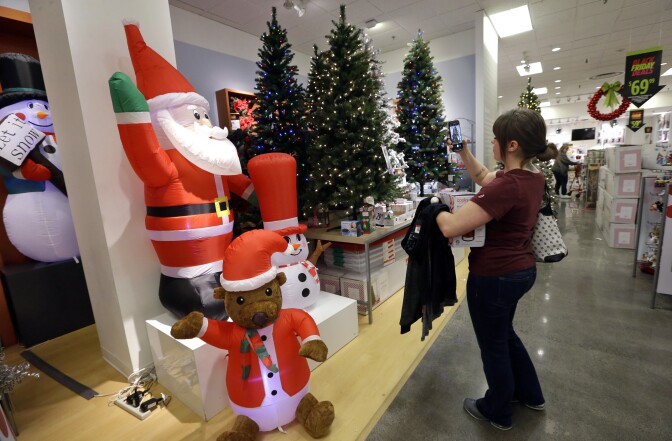 A woman in a department store takes a photo of a display of treen and blow-up yard ornaments of a Santa Claus, snowman and bear in a Santa hat.