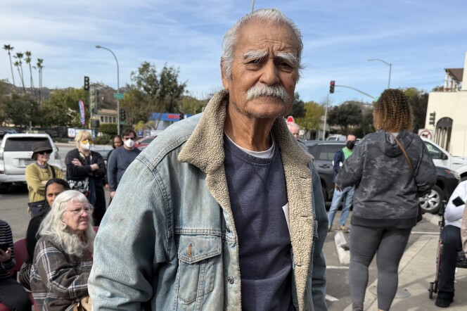 Richard Castaneda stands and waits for his mail outside the Pasadena Post Office on Lincoln Ave. His home burned down in the 2025 Eaton Fire. He wares a weathered jean jacket. He has a bushy white mustache. 