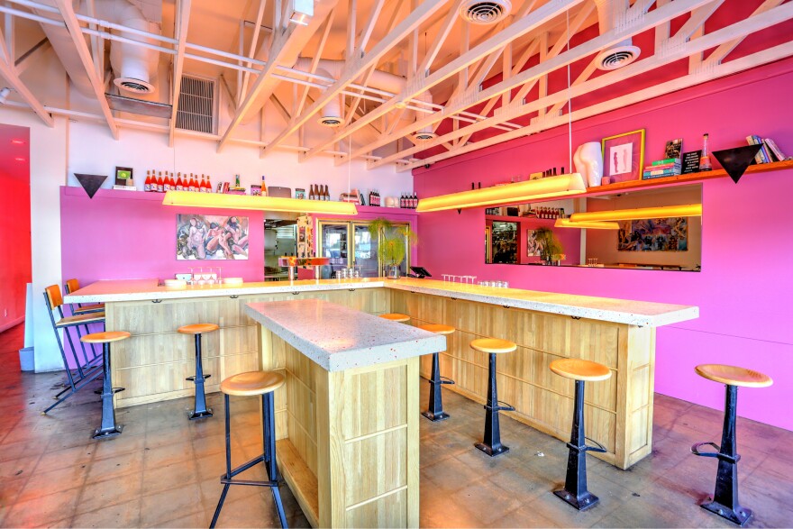 Interior of a wine bar with pink walls and exposed rafters.