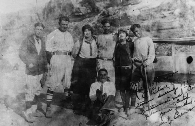 2 women stand amid 4 men in baseball uniforms and 1 man in a suit