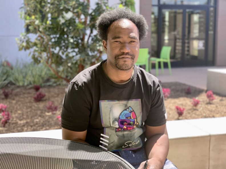 Christopher Hodge wears a graphic T-shirt and sits at an outdoor table.