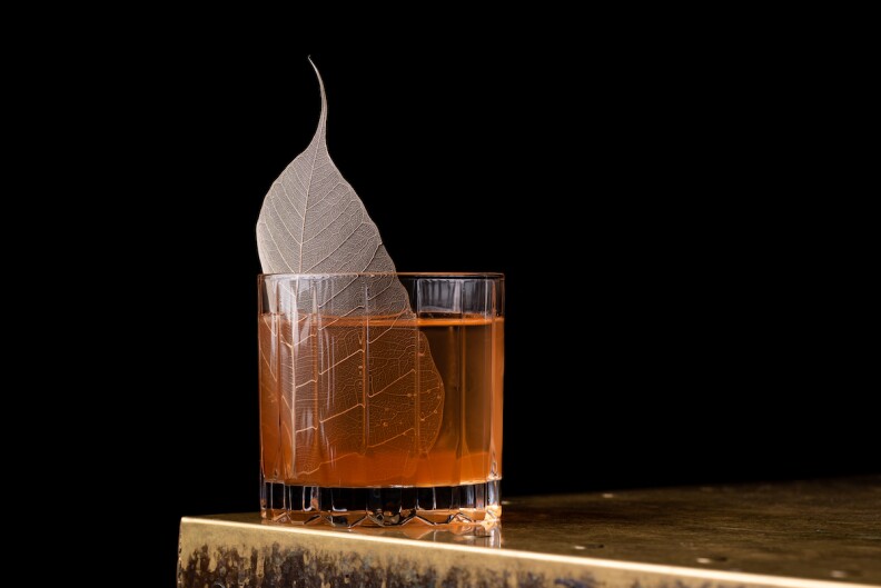 a highball glass is filled with amber liquid and one large leaf