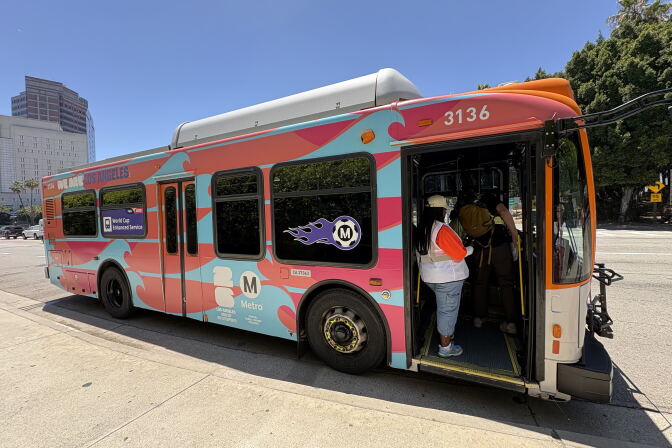 A colorful bus is parked on a curb, and a person stands at the entrance.