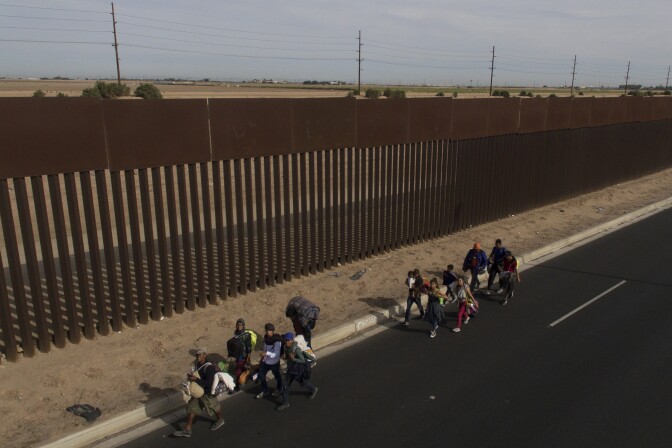 TOPSHOT - Central American migrants -mostly Hondurans- moving in a caravan towards the United States in hopes of a better life, walk along the metal fence on the border between Mexicali in Mexico's Baja California State, and Calexico, in California, US, on November 19, 2018. - US President Trump has sent about 5,800 troops to the border to forestall the arrival of large groups of Central American migrants travelling through Mexico and towards the US, in a move critics decry as a costly political stunt to galvanize supporters ahead of midterm elections earlier this month. (Photo by PEDRO PARDO / AFP)        (Photo credit should read PEDRO PARDO/AFP/Getty Images)