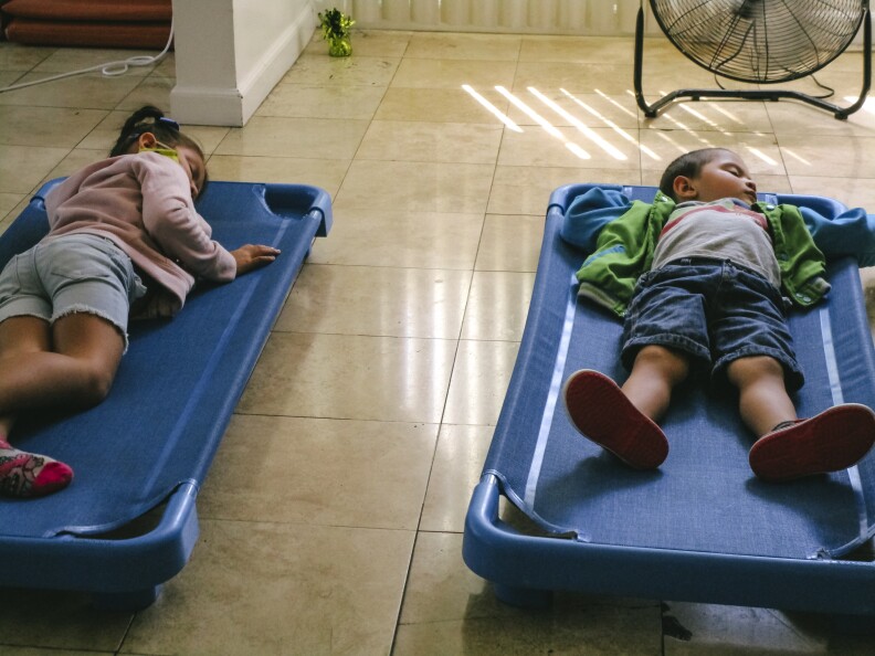In this image, two children take naps on blue cots.