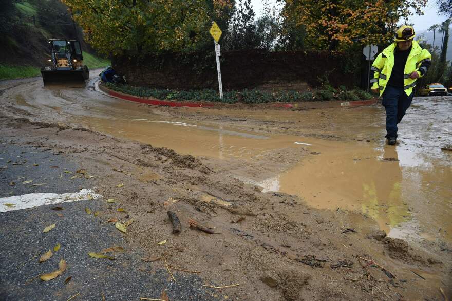 A wide view of a construction vehicle and personnel on a road that's covered in mud and brown, murky stormwater.