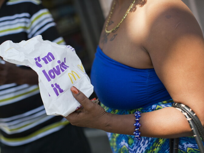 Shandelyn Rhodes holds a bag from McDonald's outside a corner store and one of Community Services Unlimited's produce stands. Rhodes likes fast food, while her her fiancé does not.