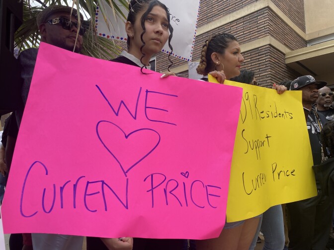 A woman is holding a pink sign that reads "We (heart symbol) Curren Price." She is in a crowd of people at a news conference where people called on the city council not to suspend Price, who is charged with public corruption.