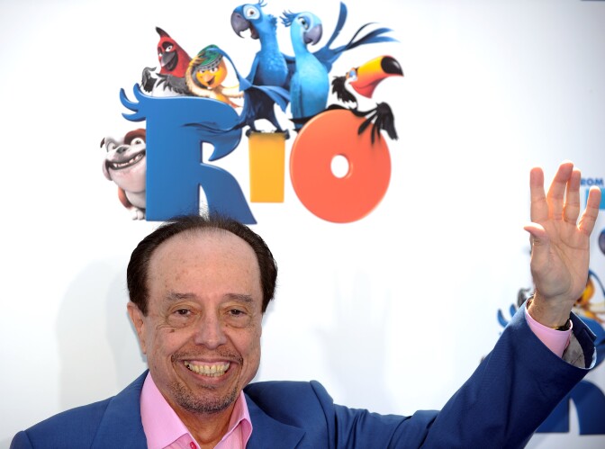 A man with medium-tone skin waves under a sign for the movie Rio.