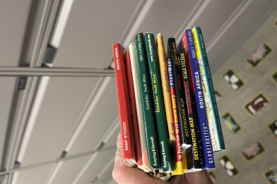 Los Angeles Public Library map librarian Peter Hauge clutches a fistful of maps of South Africa as he adds them to the Central Library's map collection. The maps come in different colors, red, white, green, yellow, black, dark blue and light blue. A row of drawers is seen in the background.