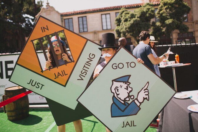 Two people dressed in costumes stand holding oversized pieces of a Monopoly board