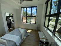 The inside of a bedroom overlooking a patio, as a woman looks toward the camera from another room.