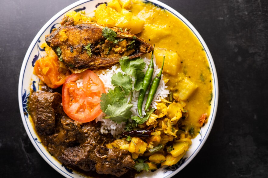 A plate of food containing fish, beef curry, and yellow lentil soup, along with white rice with a few sprigs of cilantro, and two whole green serrano peppers
