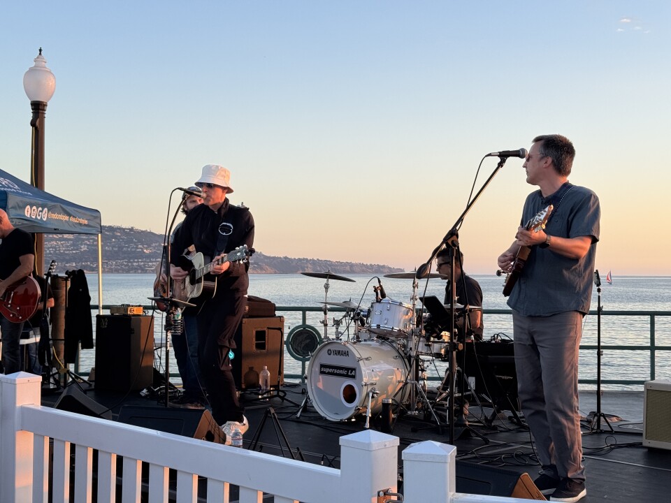 A band performs in front of an ocean and a sunset.