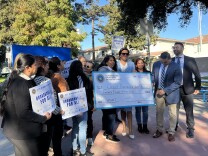 A group of people are  smiling and celebrating as they hold up a large check addressed to the city of Huntington Park.